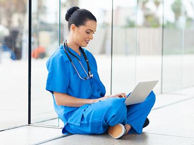 护士生坐在地板上用笔记本电脑工作.